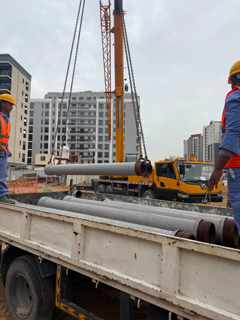 Crane loading industrial pipes onto truck at site